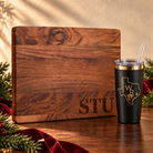 Executive gift with large black STU engraving in walnut board bottom-right corner and supplied Winding Roots WR Texas roots logo engraved in gold on black tumbler