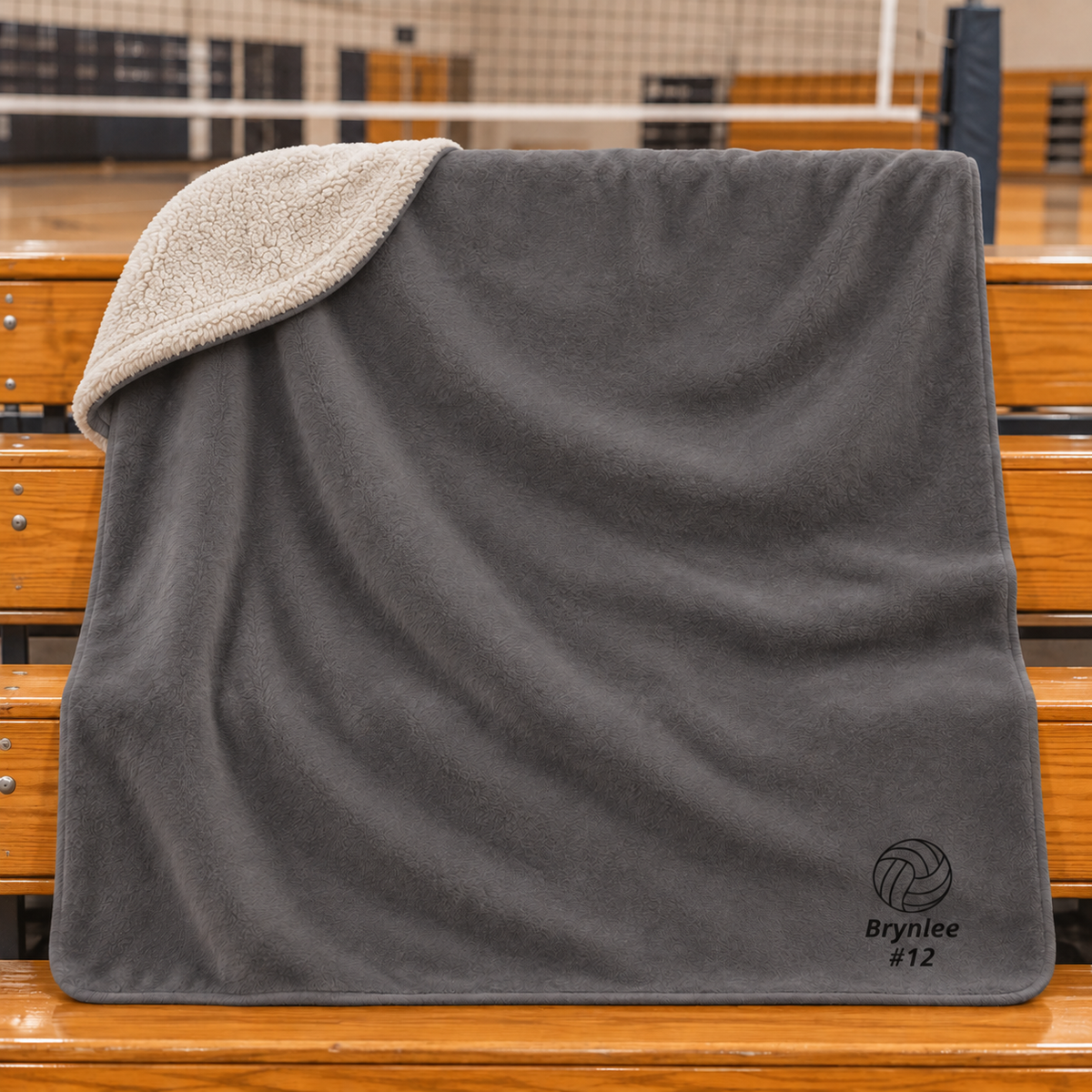 Personalized gray volleyball blanket with Brynlee number 12 and cream sherpa foldover on gym bleachers