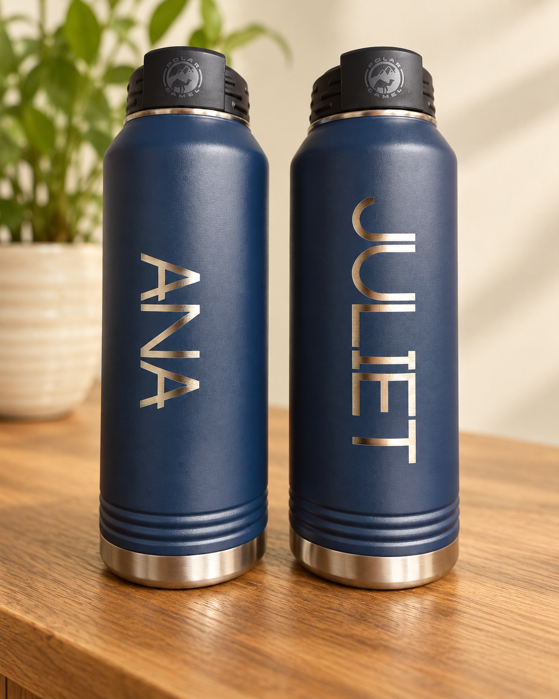 Two navy personalized water bottles engraved ANA and JULIET on a warm wood table
